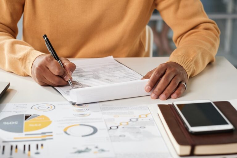 Close-up of unrecognizable black manager sitting at table and filling business document